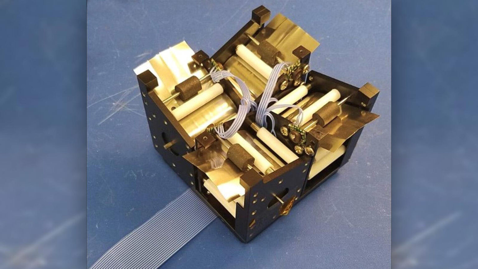 A close-up view of an electronic component assembly with a black frame, white cylindrical parts, ribbons, and wires on a blue surface.