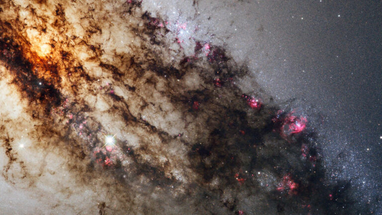 A Hubble Telescope image of a galaxy, showing a dense cluster of stars and dark bands of cosmic dust with areas of bright, glowing pink and white regions.