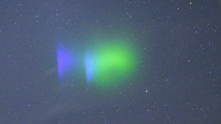 A night sky filled with stars features a bright green and blue glowing cloud-like formation near the center.