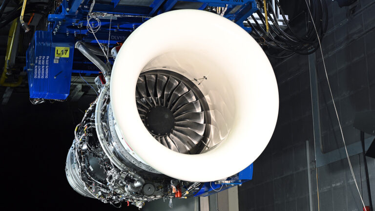 Gas turbine industry commits to sustainable aviation fuel research A close-up view of a jet engine suspended in a test facility, showcasing its front air intake and intricate internal components.