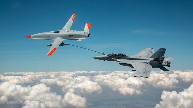 Aerial view of a military drone refueling a fighter jet mid-air above the clouds.