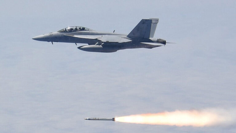 A military jet is flying in the sky and launching a missile, which is visible with a trail of fire.