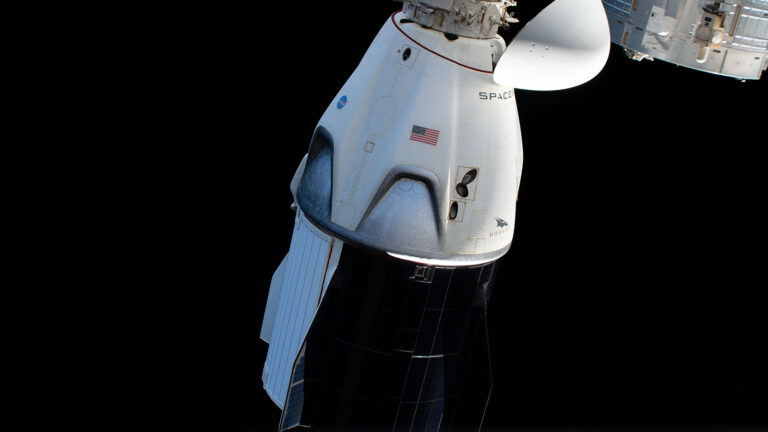 Close-up of a SpaceX Dragon spacecraft docked at the International Space Station against the backdrop of space.