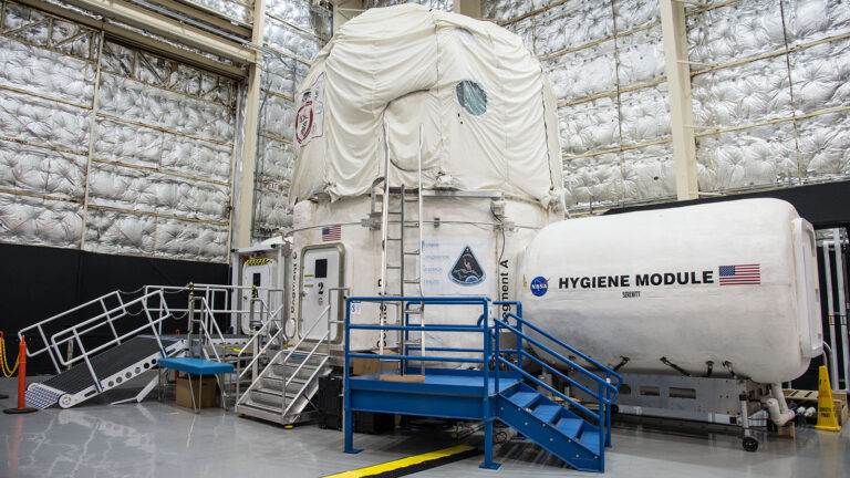 A mock-up of a space habitat with modules labeled "Hygiene Module" and "Mars Module." The setup includes access ladders and platforms inside an industrial facility.