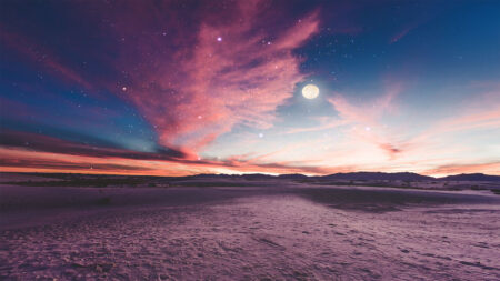 A serene desert landscape at dusk with a vibrant, colorful sky, featuring the moon and scattered stars, silhouetted mountains in the background.
