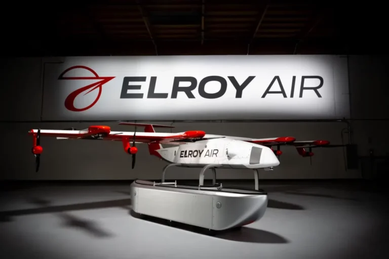 A white and red drone with the "Elroy Air" logo is displayed indoors under a large sign that reads "ELROY AIR.