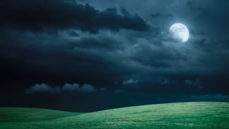 A full moon illuminates a dark, cloudy night sky above rolling green hills.