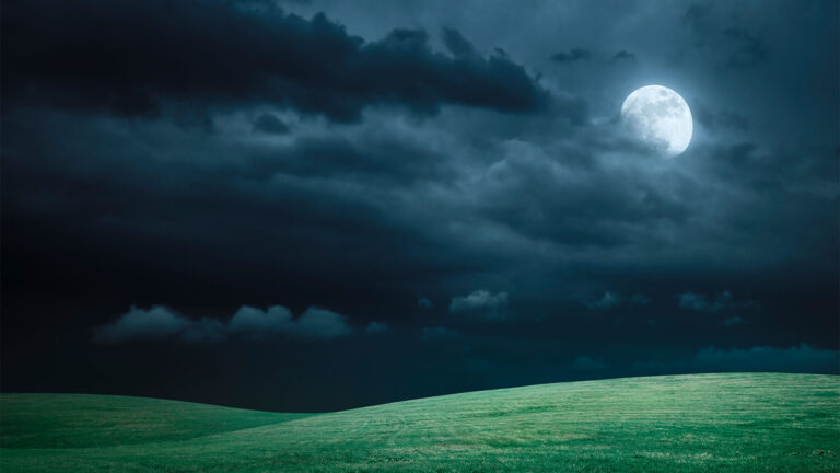 A full moon illuminates a dark, cloudy night sky above rolling green hills.