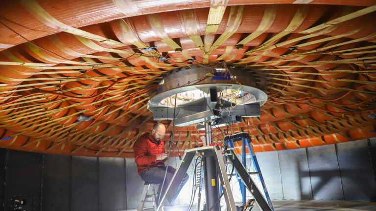 A person in a red jacket works on equipment inside a large dome-shaped structure with woven material on the ceiling.