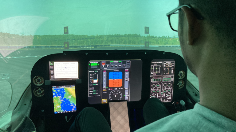 A person sits in front of a flight simulator cockpit with various digital screens and controls, looking at a virtual runway ahead.