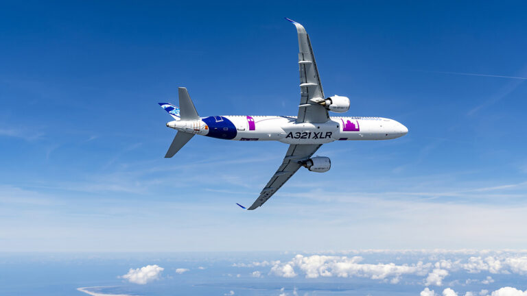 An Airbus A321XLR aircraft flying above clouds with a clear blue sky in the background. The aircraft's markings and engines are visible.