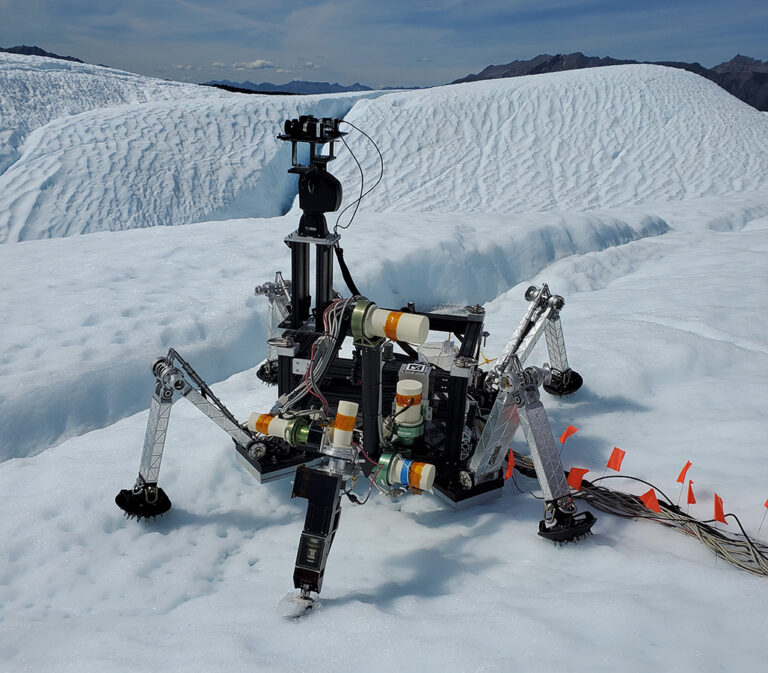 Year of autonomy in Alaskan glaciers, flight, Earth orbit, cislunar space and Mars A six-legged robot equipped with sensors, wires, and cameras is positioned on a snowy landscape with mountainous terrain in the background.