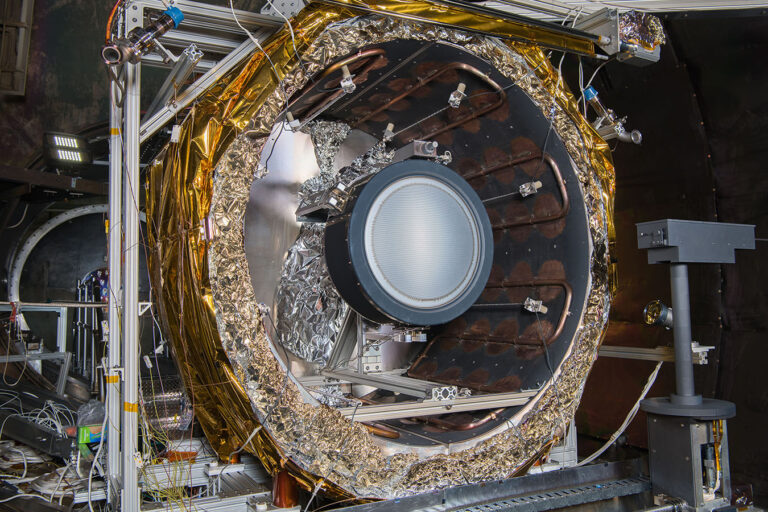Variety grows and performance improves in space electric propulsion A close-up view of a gold-wrapped James Webb Space Telescope instrument inside a test chamber, surrounded by various technical equipment and cables.