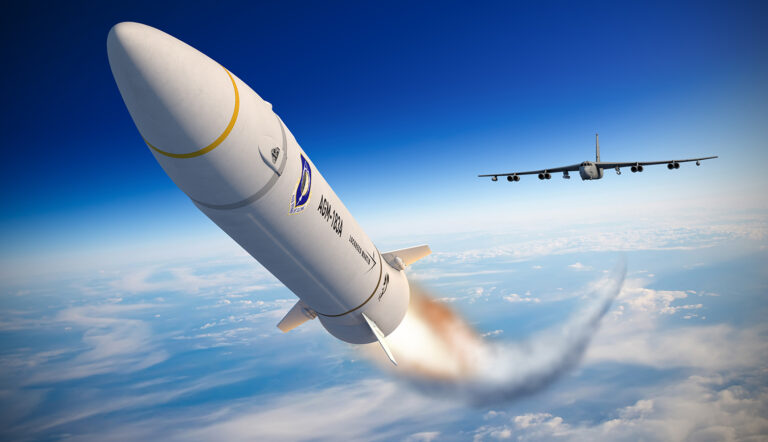 Race for hypersonics spurs on missile systems A missile is fired into the sky with a trail of smoke behind it, while a military aircraft flies in the background against a blue sky and cloud backdrop.