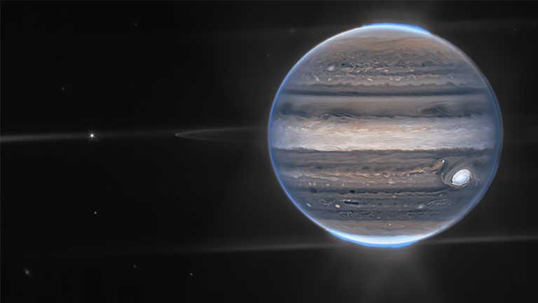 Image of Jupiter with its Great Red Spot and several bands of clouds, captured in high detail. The planet's thin rings are faintly visible, and the background is a dark space with a few distant stars.