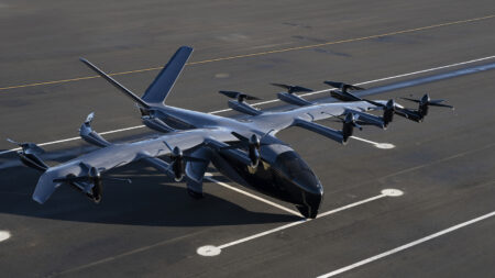 A sleek, black electric vertical takeoff and landing (eVTOL) aircraft with multiple rotors is parked on an airstrip.