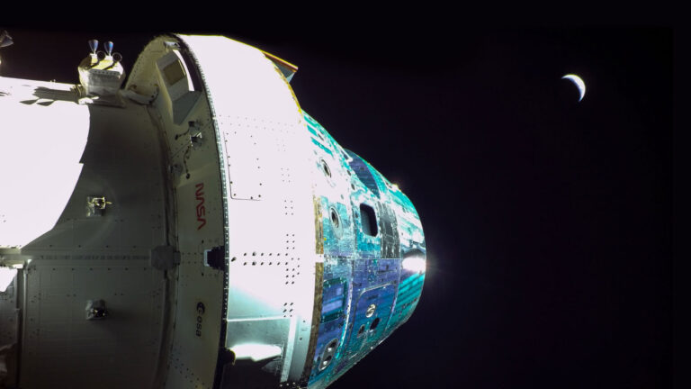 Close-up of a spacecraft with the NASA logo visible, set against the dark backdrop of space with a crescent moon in the distance.