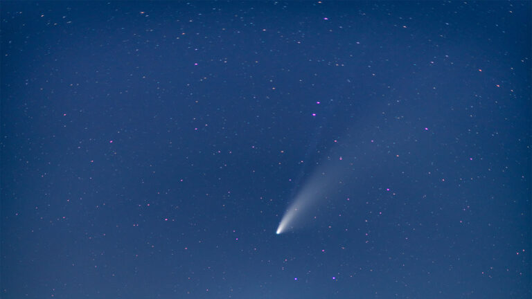 A bright comet with a prominent tail is visible against a star-filled night sky.