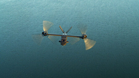 A tiltrotor aircraft in flight over a body of water, with its rotors in a horizontal position.