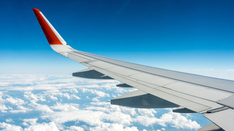 View of an airplane wing with red tip against a blue sky and clouds below.