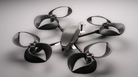 A black quadcopter drone with four large propellers is displayed on a gray surface.