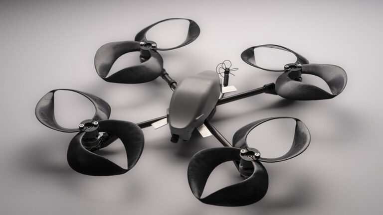 A black quadcopter drone with four large propellers is displayed on a gray surface.