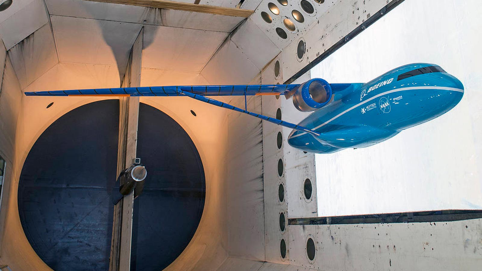 A scale model of a blue aircraft with an elongated tail is tested in a wind tunnel.