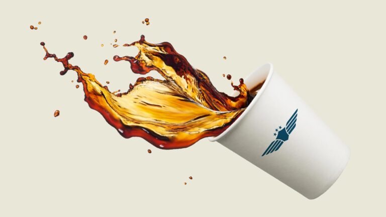 A white paper cup with a logo spills coffee mid-air, creating a dynamic splash against a plain background.