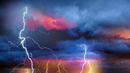 A stormy sky with dark clouds is illuminated by multiple lightning bolts and vibrant colors, including shades of blue, pink, and orange.