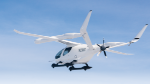 A white electric aircraft with the propeller at the rear is flying in a clear blue sky. The identification number N250UT is visible on the tail.