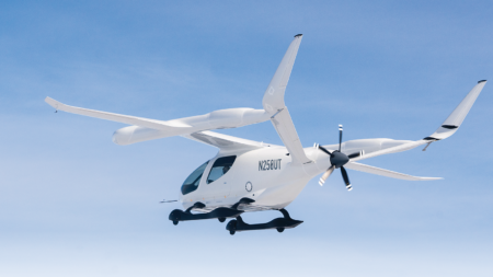 A white electric aircraft with the propeller at the rear is flying in a clear blue sky. The identification number N250UT is visible on the tail.