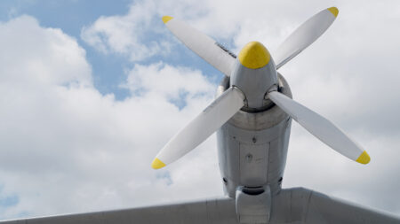 Close-up view of the propeller and engine of an airplane against a backdrop of a partly cloudy sky.