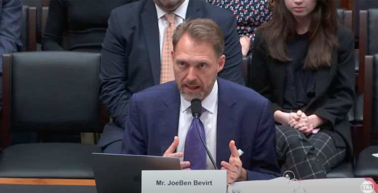 A man in a suit and tie speaks passionately at a hearing, seated behind a microphone and nameplate that reads "Mr. JoeBen Bevirt." There are several people seated behind him.
