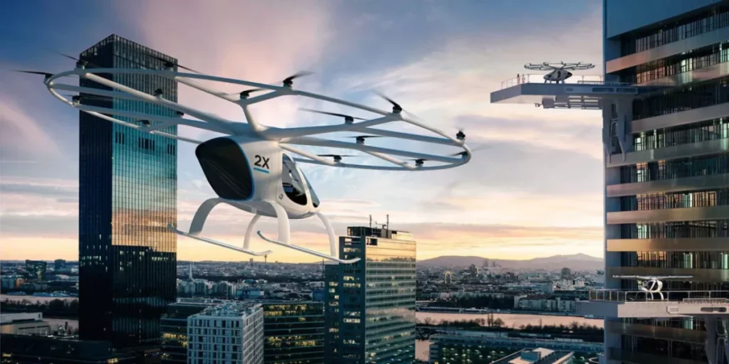 A white drone-like air taxi is flying near a high-rise building at dusk in a city, with another similar vehicle visible in the background.