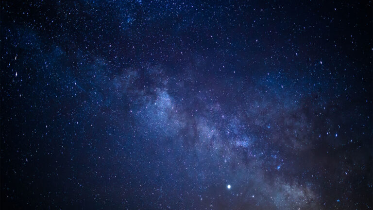 A night sky filled with countless stars and the Milky Way galaxy visible as a cloudy band across the middle.