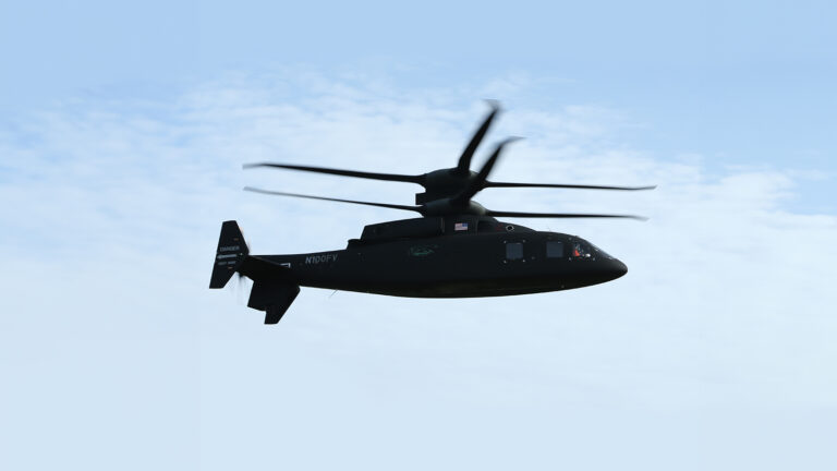A black helicopter with dual rotors is flying against a blue sky with scattered clouds.