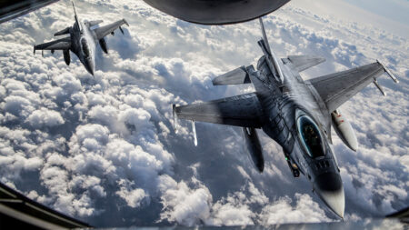 Two military fighter jets flying side by side above clouds, viewed from above.