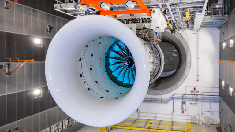 A close-up view of a large aircraft engine in a testing facility, showcasing the front intake and internal fan blades.