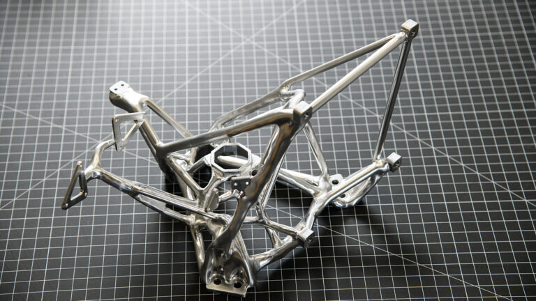 A polished metal frame structure is displayed on a black and white grid-patterned surface.