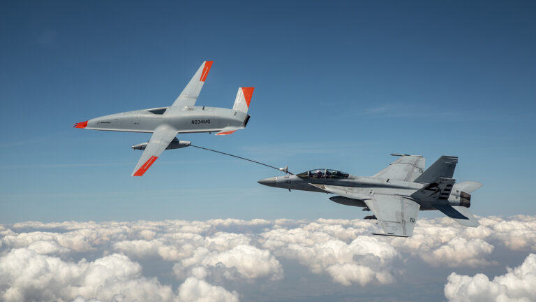 A military drone refuels a fighter jet mid-air above the clouds.