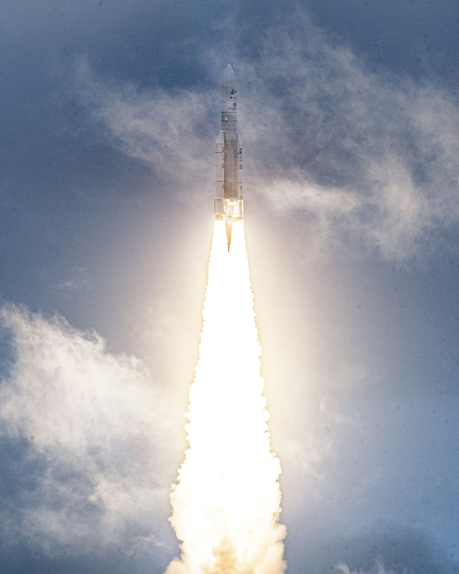 A rocket is launching vertically into the sky, emitting bright flames and a trail of smoke against a cloudy backdrop.