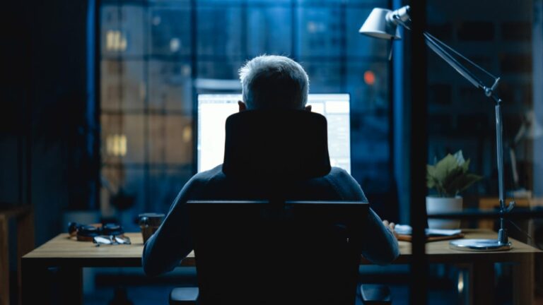 Silhouette of a man sitting in front of a computer screen