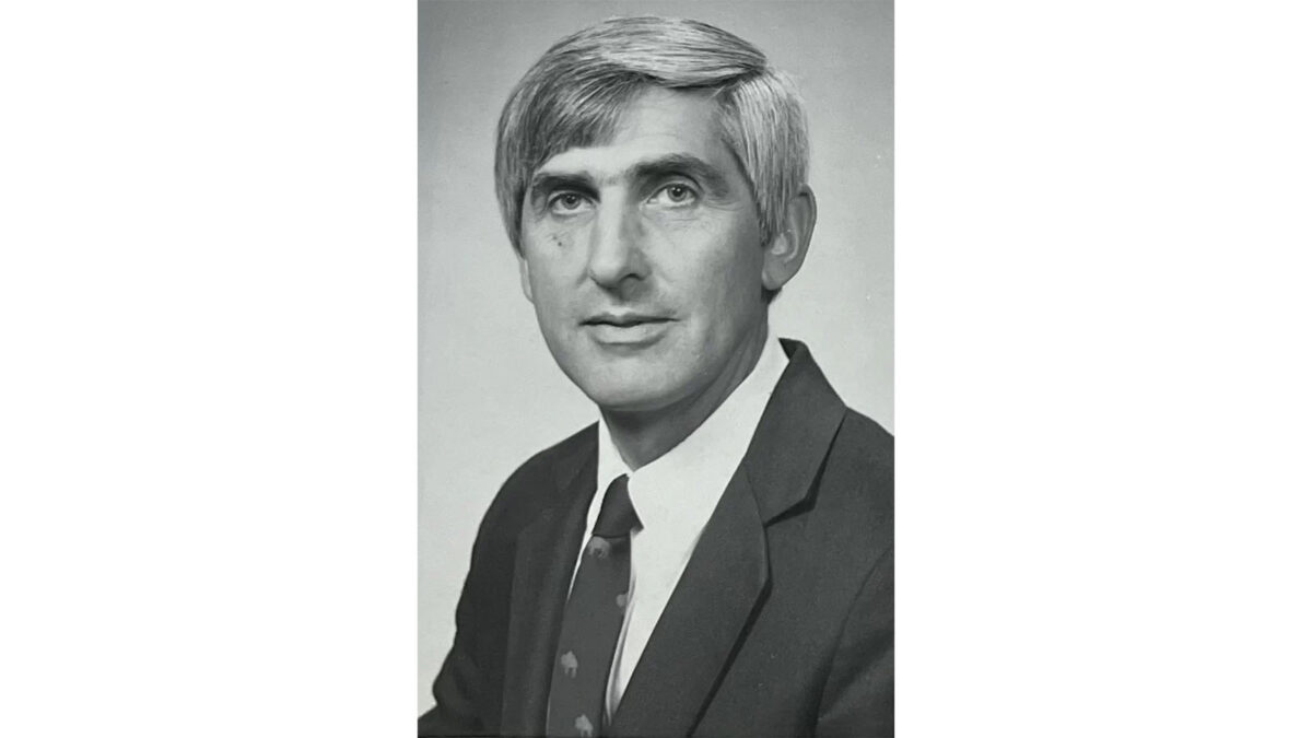 Black and white portrait of a man with short, silver hair in a suit and tie, gazing directly at the camera.