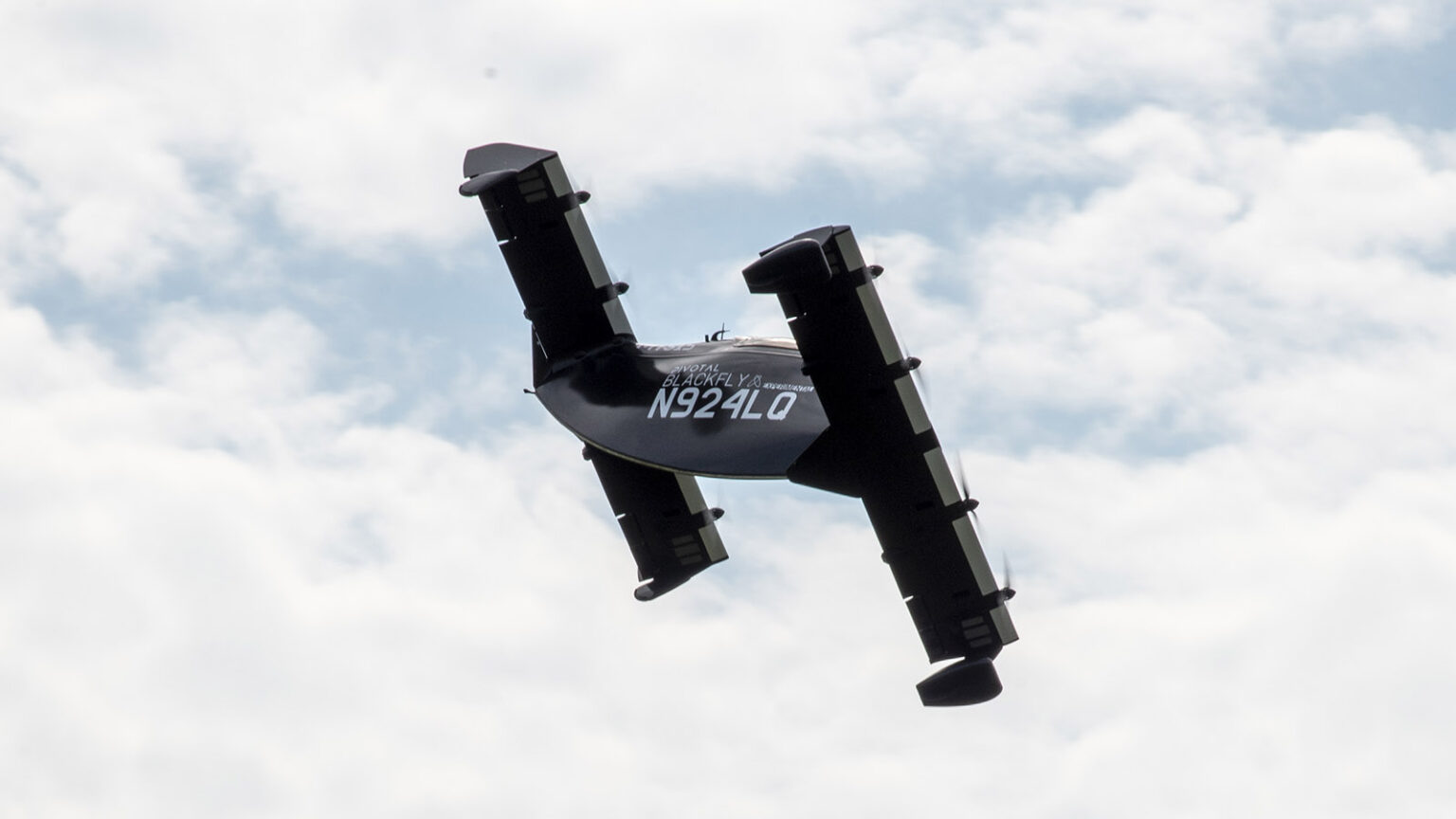 A black aircraft with the registration number N924Q is flying at an angle against a cloudy sky.