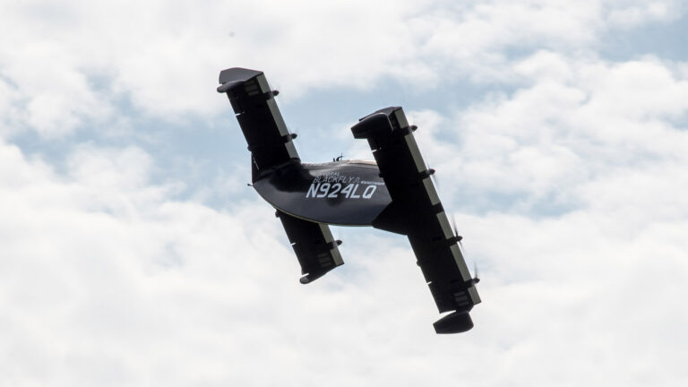A black aircraft with the registration number N924Q is flying at an angle against a cloudy sky.