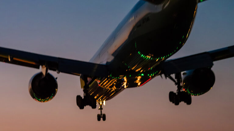 A commercial airplane approaches for landing at dusk with its landing gear extended and lights illuminated.