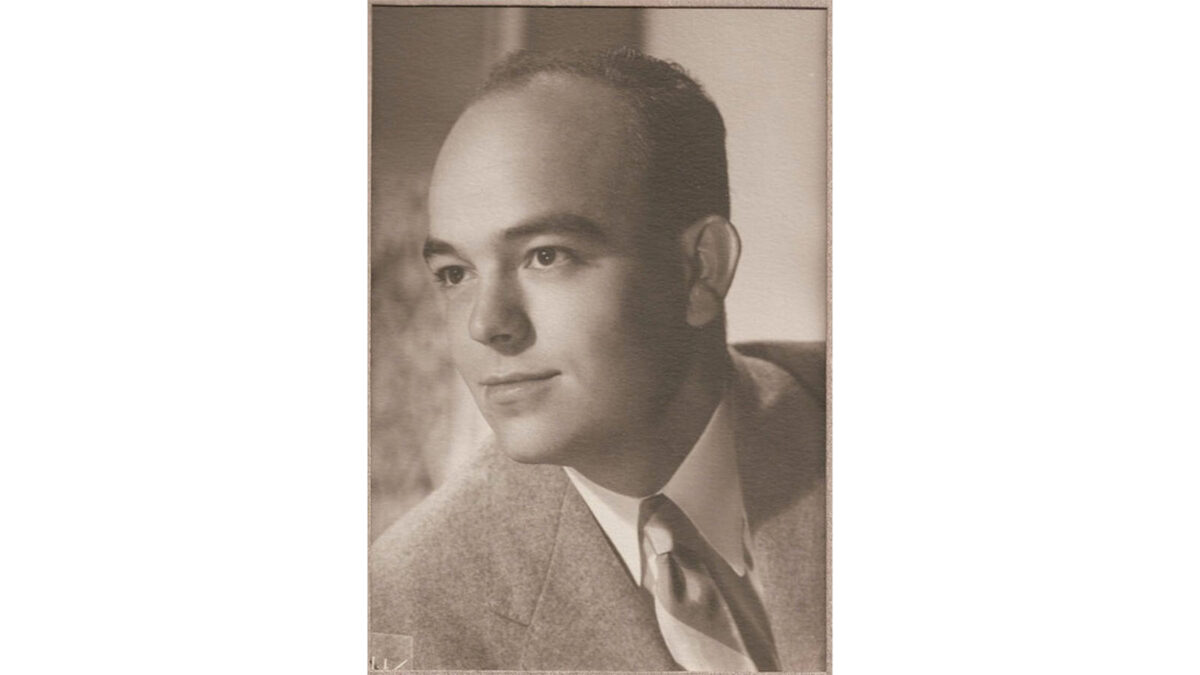 Black and white portrait of a man in a suit and tie, looking to the side with a neutral expression.