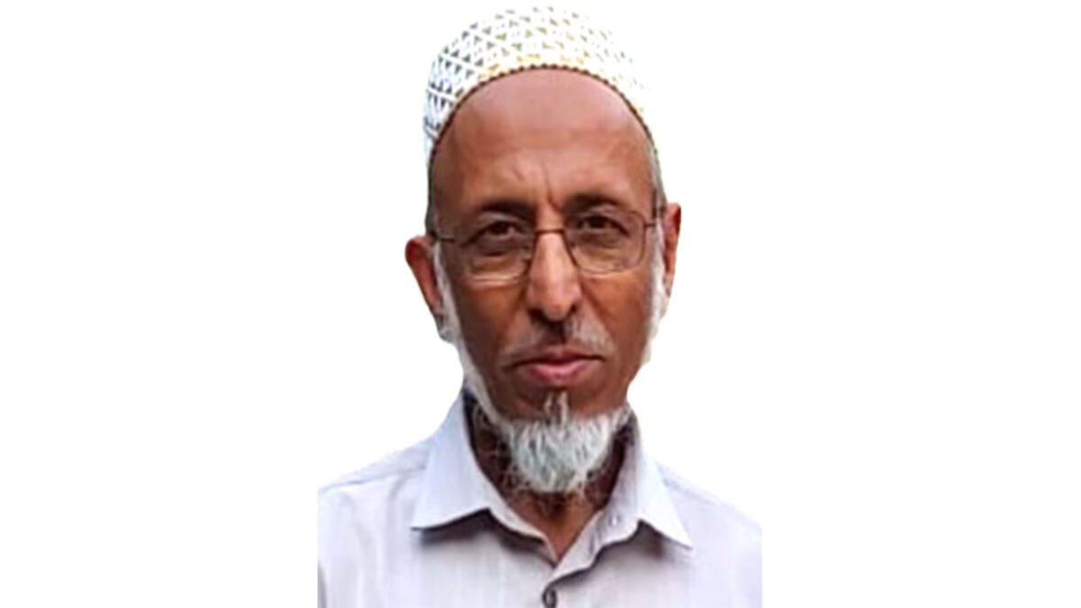 A man with glasses and a white beard, wearing a white cap and light grey shirt, stares at the camera against a plain white background.