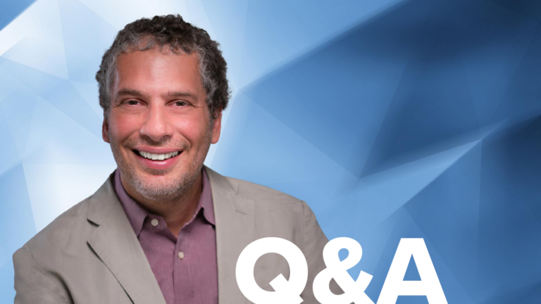 A smiling man in a beige jacket and maroon shirt is set against a blue geometric background. The letters "Q&A" are in the bottom right corner.