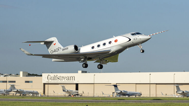 A Gulfstream G400 aircraft taking off from an airport runway with a hangar and other planes in the background.